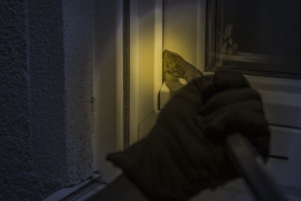 Image of a burglar prying open a window at night